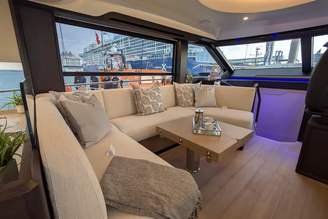 Luxurious yacht interior with a sofa, decorative cushions, and a glass view of a cruise ship docked nearby.